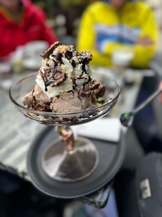 A glass dish with ice cream and chocolate toppings

Description automatically generated