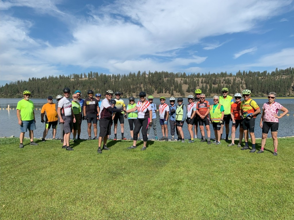 A group of people standing on grass by water

Description automatically generated