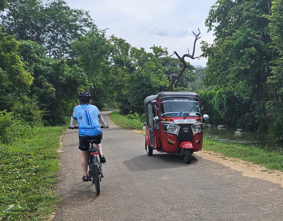 A person riding a bicycle on a road with a tuk

Description automatically generated