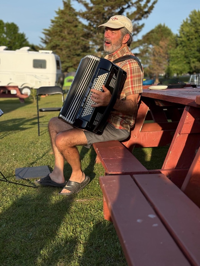 A person sitting on a picnic table playing an accordion

Description automatically generated